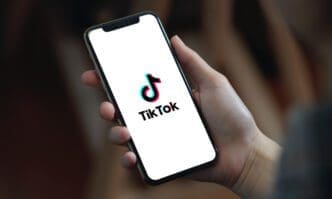 A person is holding a smartphone displaying the TikTok logo on its screen