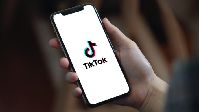 A person is holding a smartphone displaying the TikTok logo on its screen