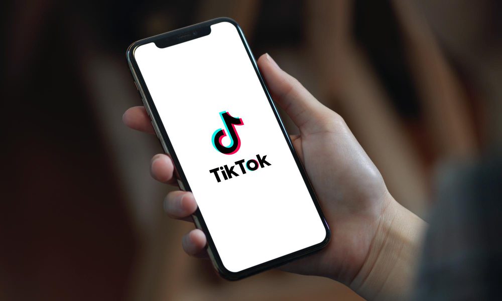 A person is holding a smartphone displaying the TikTok logo on its screen