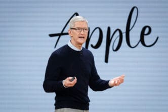 Tim Cook speaking on stage at an Apple event with the Apple logo behind him