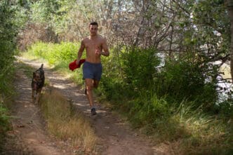 A man and his dog run down a dirt trail surrounded by greenery