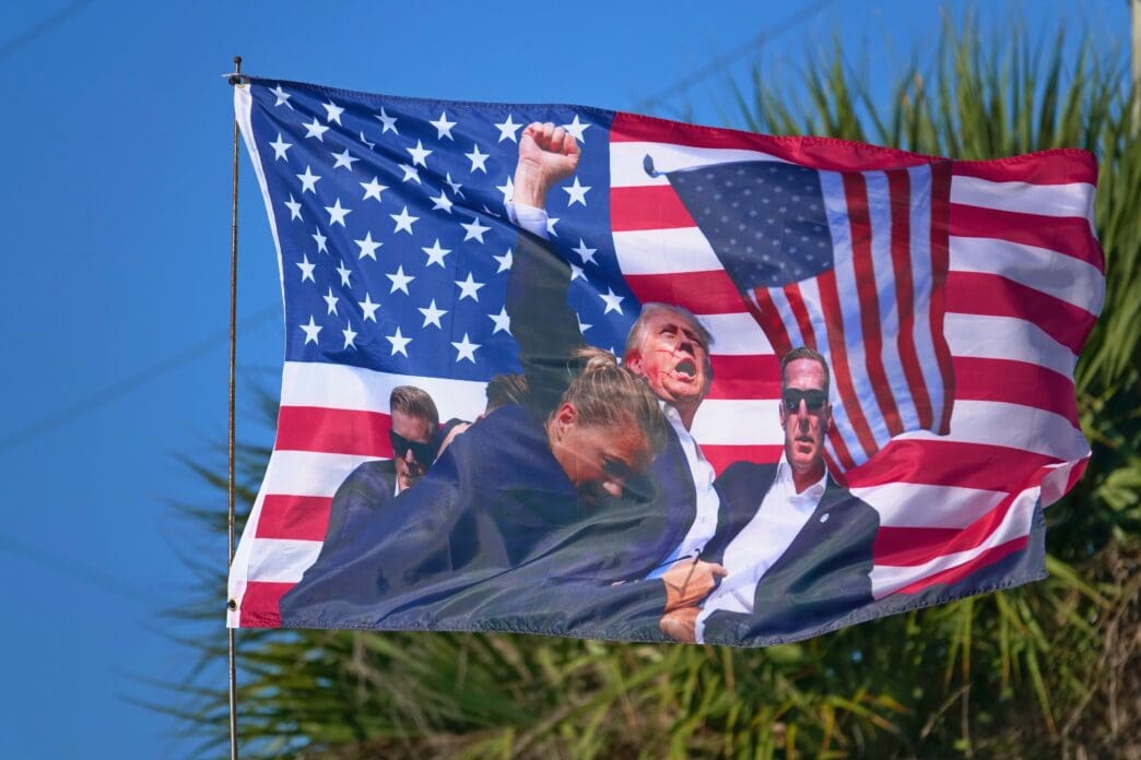 American flag with images of Donald Trump and others, waving against a blue sky
