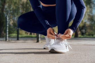 A woman in athletic clothes crouches down to tie the laces of her white running shoes