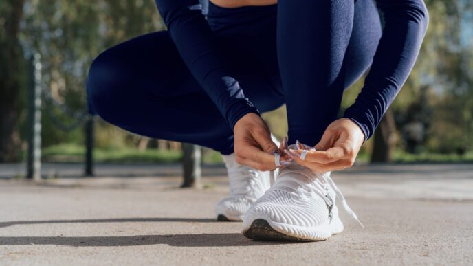 A woman in athletic clothes crouches down to tie the laces of her white running shoes