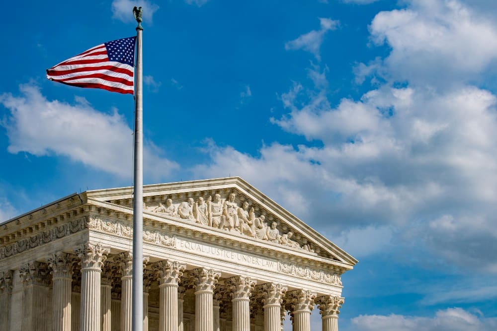 The American flag flies high on a flagpole over the facade of the U.S. Supreme Court building