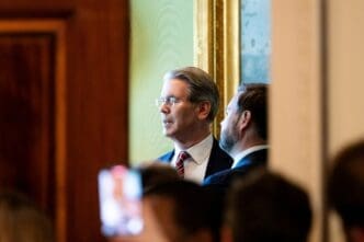 U.S. Treasury Secretary Scott Bessent peers into the distance, with another man and a crowd visible behind him, at a press conference