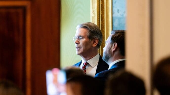 U.S. Treasury Secretary Scott Bessent peers into the distance, with another man and a crowd visible behind him, at a press conference