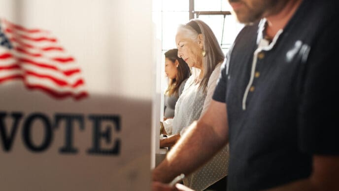 People are casting their votes inside voting booths, with a sign that reads VOTE and an American flag visible.