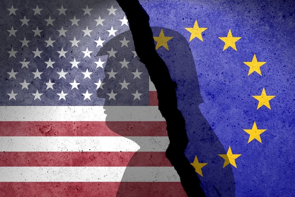 The American and European Union flags are shown on a cracked concrete wall with silhouettes of heads