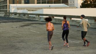 Three people run on a city street with skyscrapers in the background