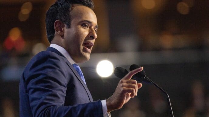 Vivek Ramaswamy, in a suit and tie, speaks passionately into a microphone at a political event