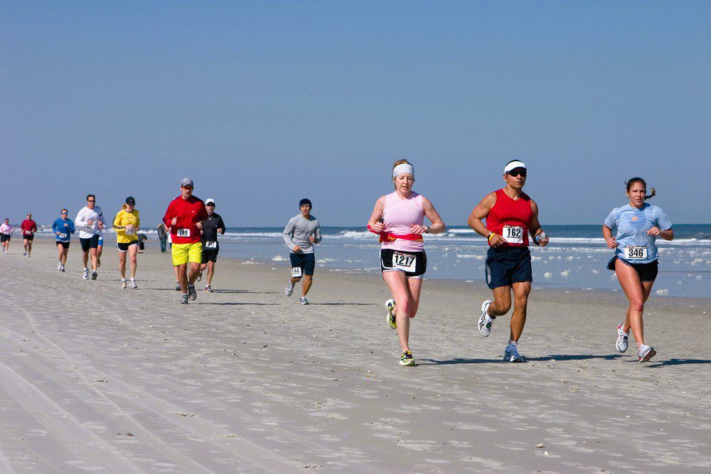 Runners in a race on a sandy beach under a clear, blue sky