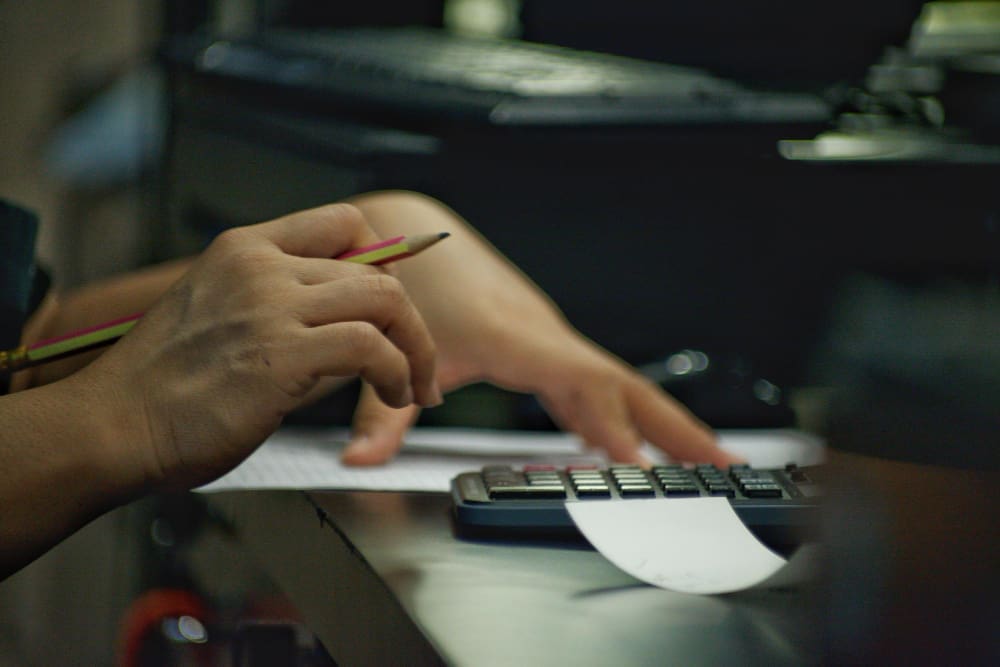 A person’s hands using a calculator and a pencil, with papers on a desk