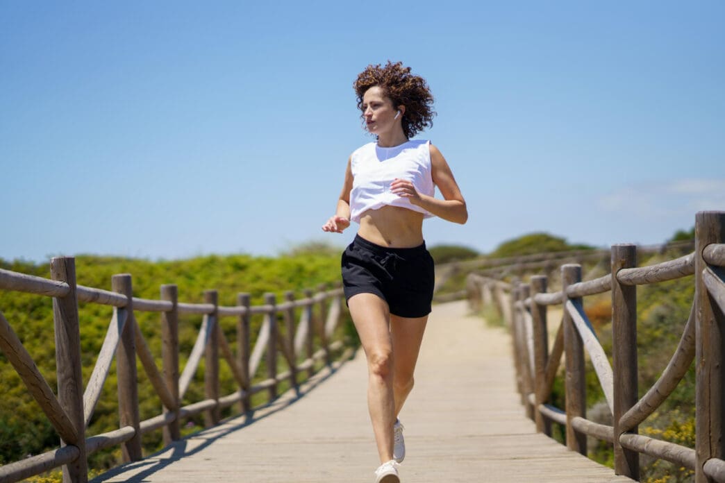 A young woman with curly hair jogs on a wooden boardwalk on a sunny day