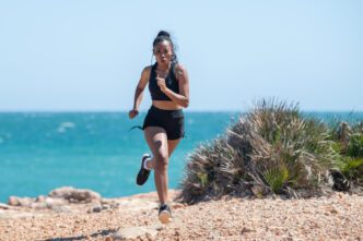 A woman running in black workout clothes on a rocky trail with the ocean in the background