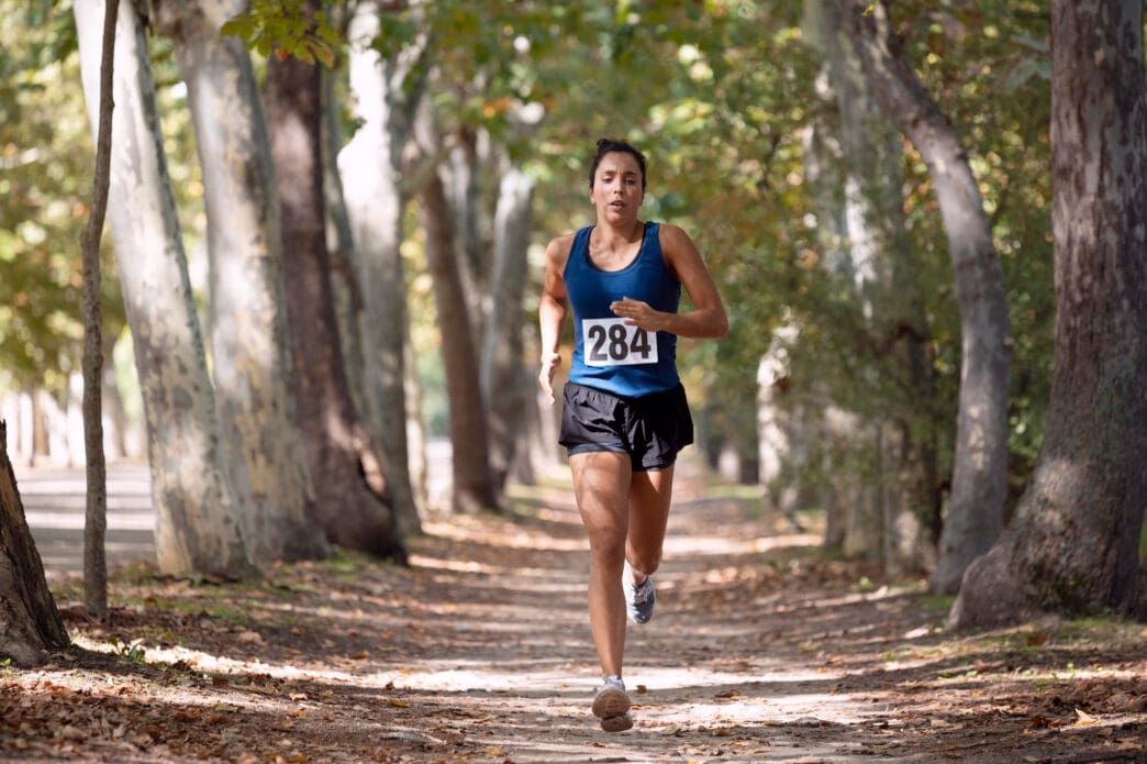 A woman with bib number 284 runs on a tree-lined dirt path