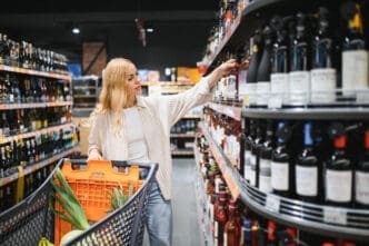 Woman choosing a bottle of wine from a shelf in a supermarket
