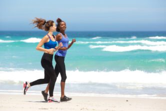 Two women in athletic wear running and smiling on a sunny beach in Miami
