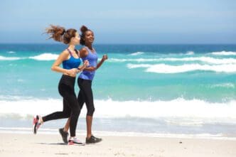 Two women in athletic wear running and smiling on a sunny beach in Miami