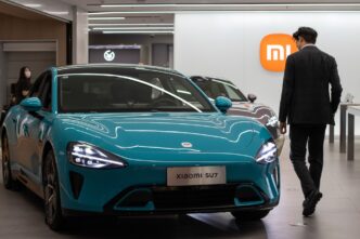 The electric Xiaomi SU7 car is displayed in a showroom with a person walking past it