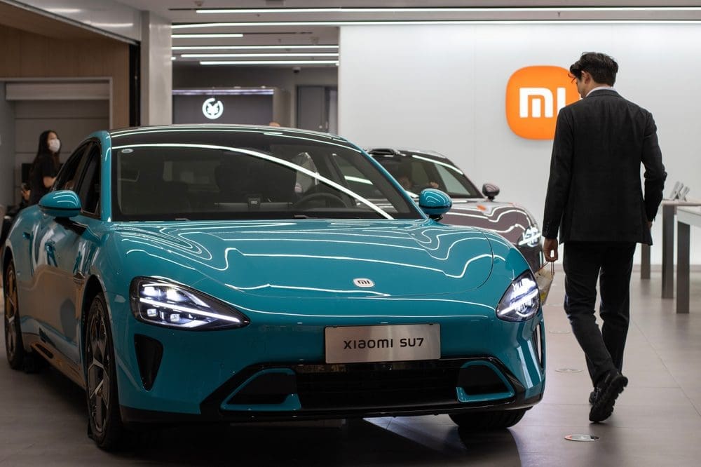 The electric Xiaomi SU7 car is displayed in a showroom with a person walking past it