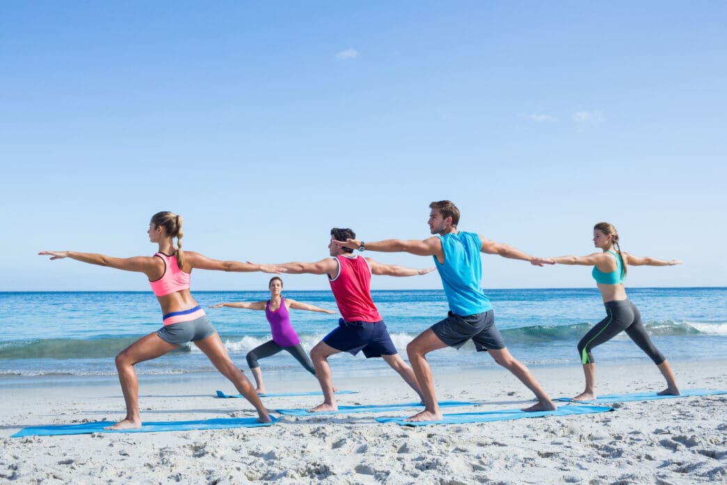 Group of people practicing yoga on a beach at the sea