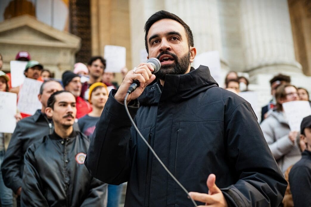 New York State Assemblymember Zohran Mamdani speaks into a microphone at a political rally in Bryant Park
