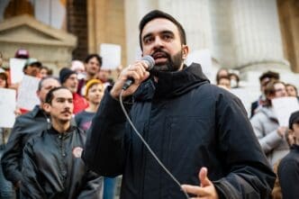 New York State Assemblymember Zohran Mamdani speaks into a microphone at a political rally in Bryant Park