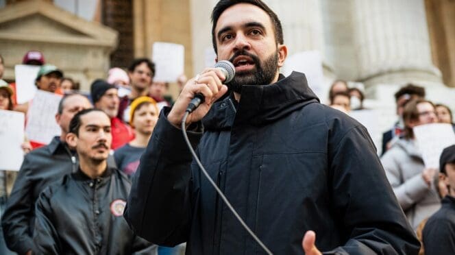 New York State Assemblymember Zohran Mamdani speaks into a microphone at a political rally in Bryant Park