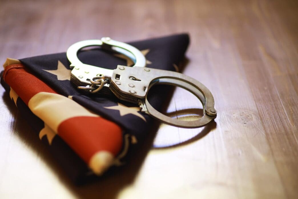 An American flag rests beside a pair of handcuffs on a wooden surface, symbolizing justice and patriotism.