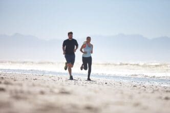 A man and woman run on a beach, likely during a vacation, emphasizing fitness and wellness.