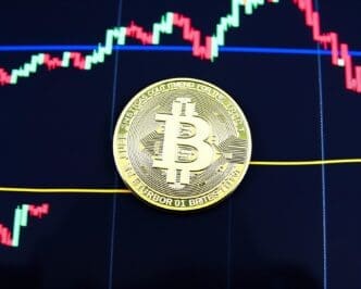 A physical Bitcoin coin rests on a stock market chart, representing cryptocurrency trading.