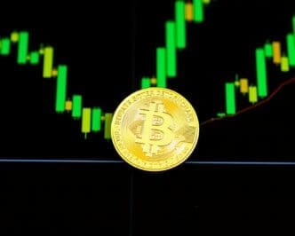 A gold Bitcoin coin rests on top of a price chart.