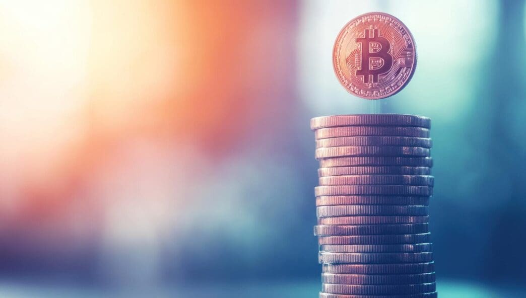 Bitcoin symbol rising above a stack of coins, with a city skyline in the background, representing finance.