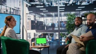 Two business associates analyze key performance indicators (KPIs) on a device screen, set against a plain background.