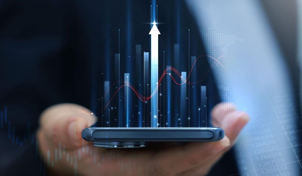 Businessman holding a smartphone displaying a glowing stock market chart with an upward arrow, representing financial growth and investment success.