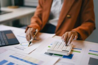 Businesswoman in an office setting analyzes financial charts and uses a calculator.