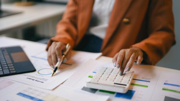 Businesswoman in an office setting analyzes financial charts and uses a calculator.