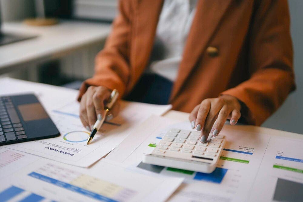Businesswoman in an office setting analyzes financial charts and uses a calculator.