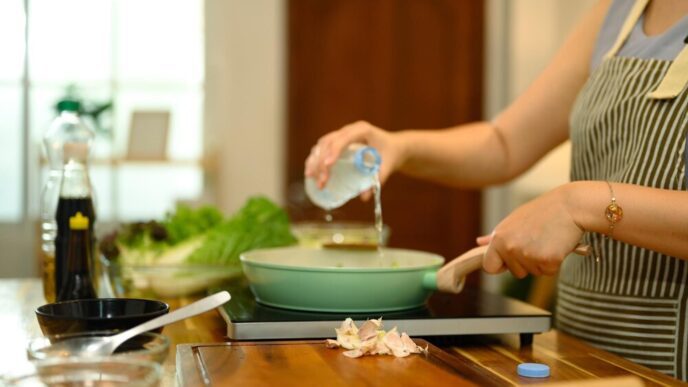 Close-up of a woman pouring water into a pan on an induction stove while cooking.