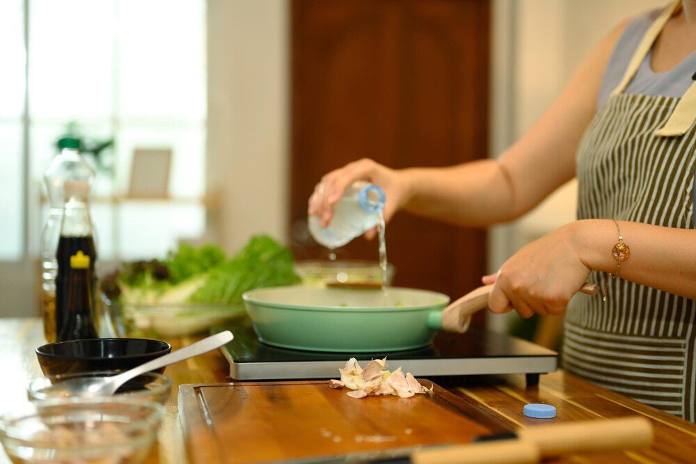 Close-up of a woman pouring water into a pan on an induction stove while cooking.