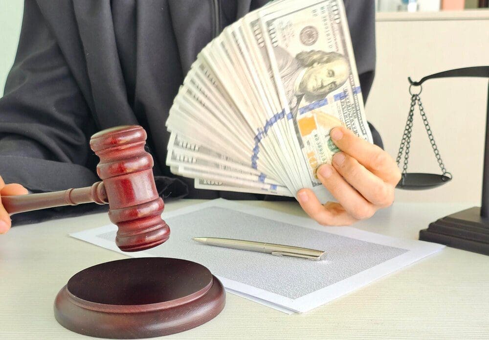 A gavel rests on a table with cash in hand during a courtroom legal proceeding.
