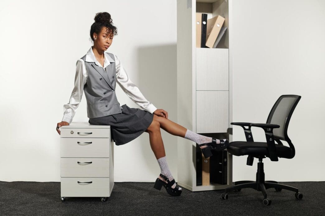 A young woman in business attire stands confidently in a modern office setting.