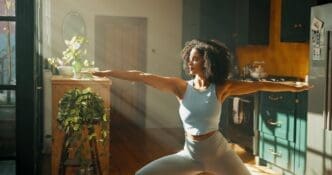 Woman in a home apartment practices yoga, stretching, and the warrior pose as part of a wellness routine.