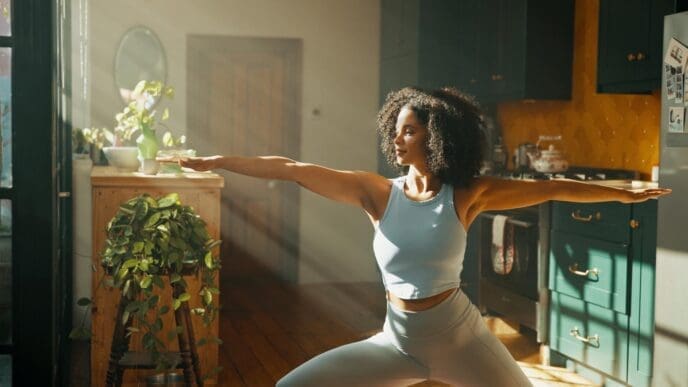 Woman in a home apartment practices yoga, stretching, and the warrior pose as part of a wellness routine.