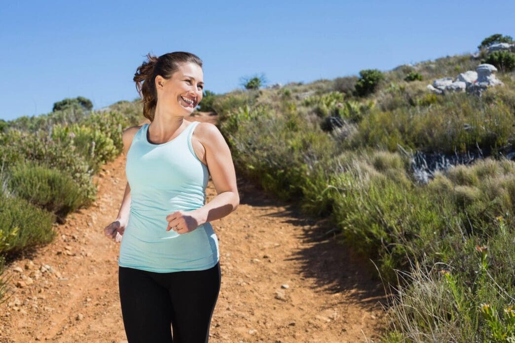Smiling couple jogs down a mountain trail.
