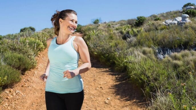 Smiling couple jogs down a mountain trail.