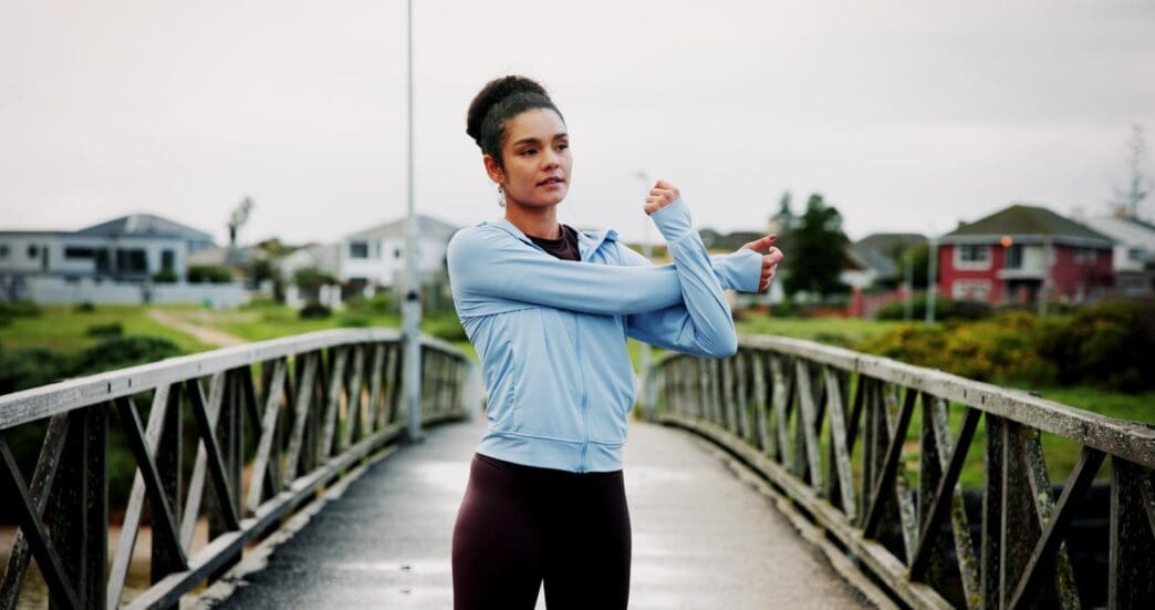 Woman stretching on a bridge, preparing for a morning cardio routine in a park.