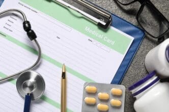 Flat lay of a medical card, pills, and a stethoscope on a grey, textured surface.