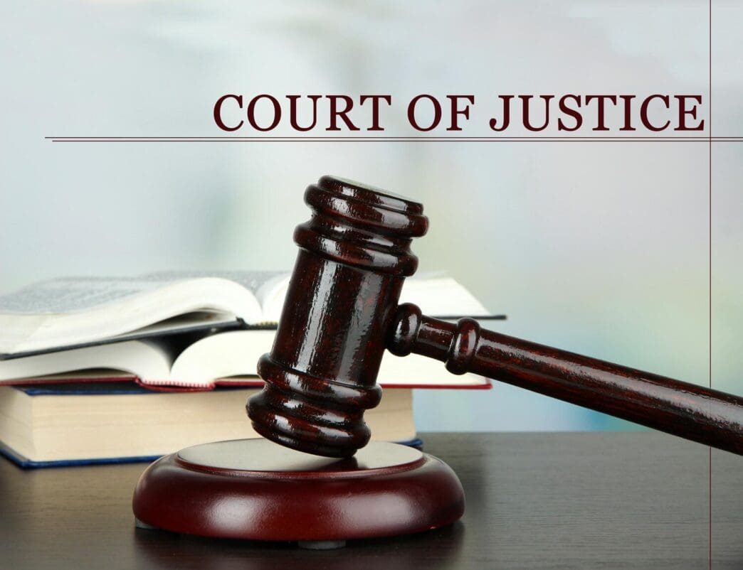 A gavel rests on a table beside a stack of books, all against a light background.